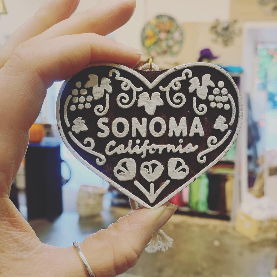 A black heart-shaped ornament carved with Sonoma California, held up in the shop